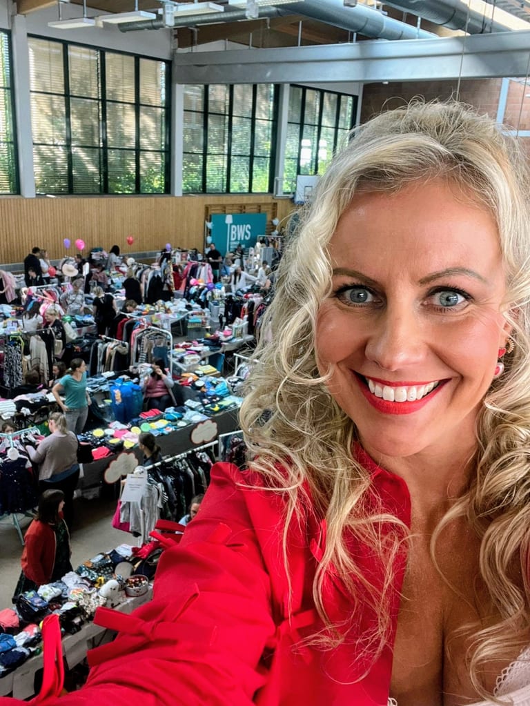 Kathleen im roten Blazer lacht in die Kamera, dahinter die volle Flohmarkthalle